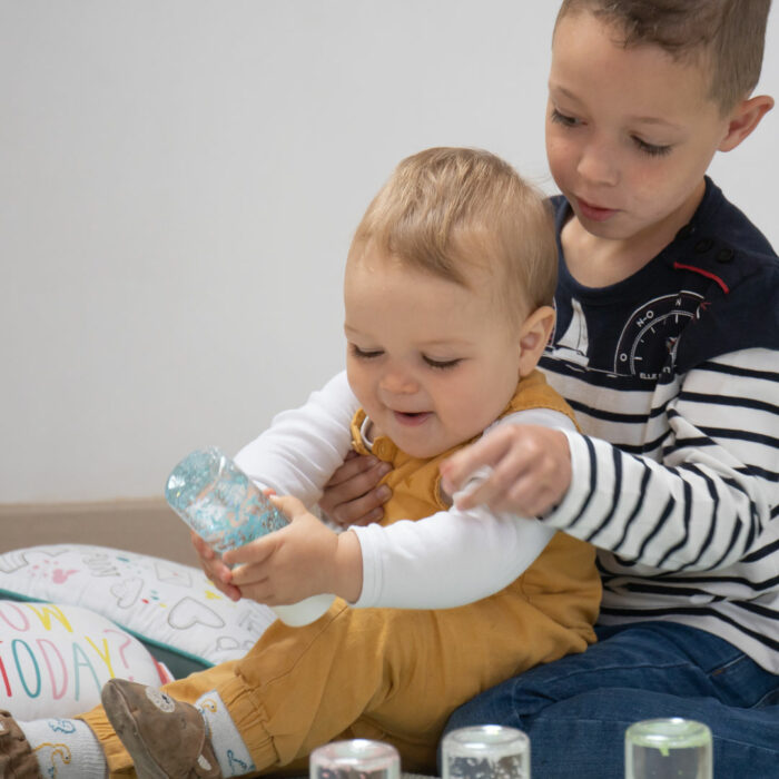 Bébé manipulant une bouteille sensorielle avec son grand frère, jouet d’éveil sécurisé et apaisant.
