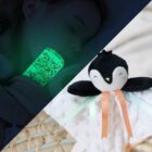 Bébé endormi tenant une bouteille sensorielle phosphorescente, avec un doudou émotions posé à côté pour un sommeil rassurant.