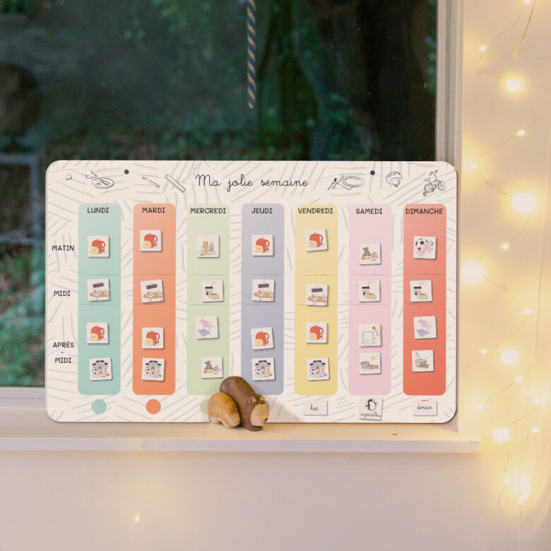 Tableau magnétique Ma jolie semaine édition Noël de l’Atelier Gigogne posé sur un rebord de fenêtre illuminé, pour aider les enfants à se repérer dans le temps avec douceur et magie.
