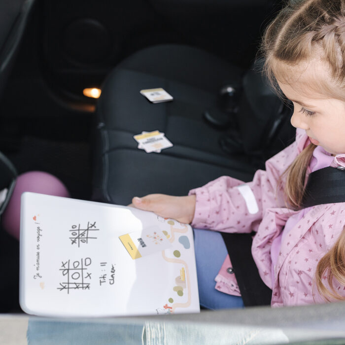 Enfant jouant avec le tableau effaçable du kit Je m’amuse en voyage dans la voiture, pour s’occuper et apprendre sur la route.