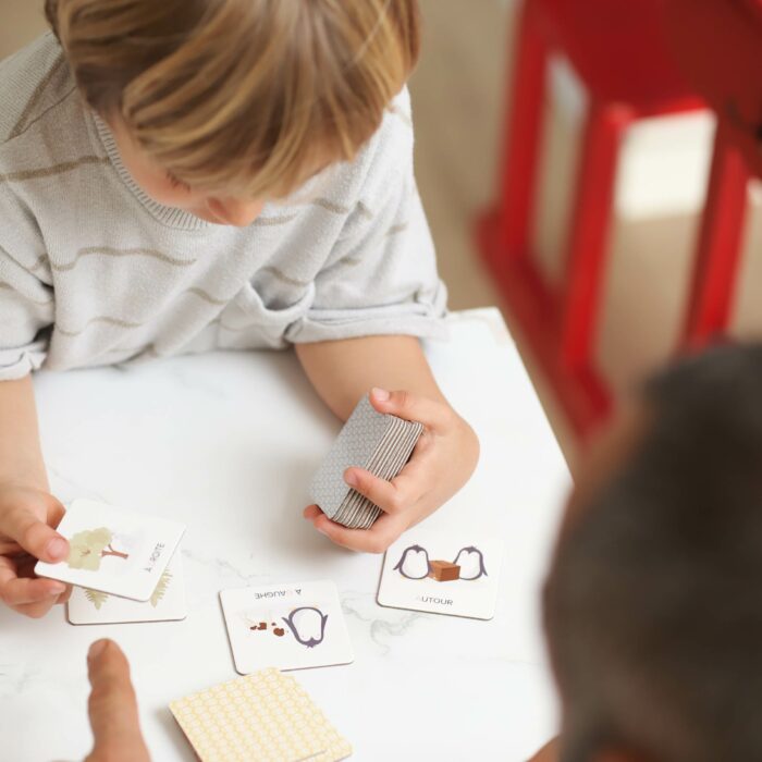 Enfant jouant à un jeu de repérage spatial avec un adulte à l’aide de cartes illustrées.