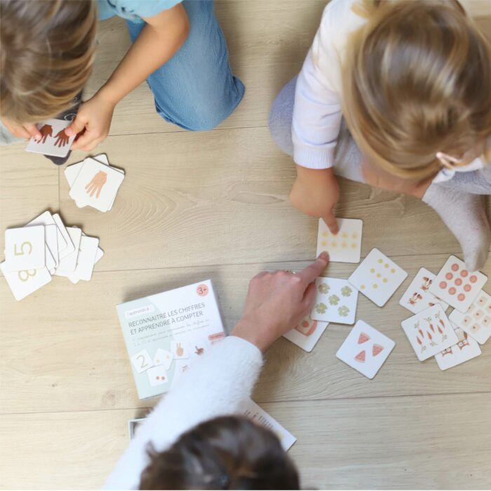 Enfants apprenant à compter avec un jeu de cartes éducatif, accompagnés d’un adulte.