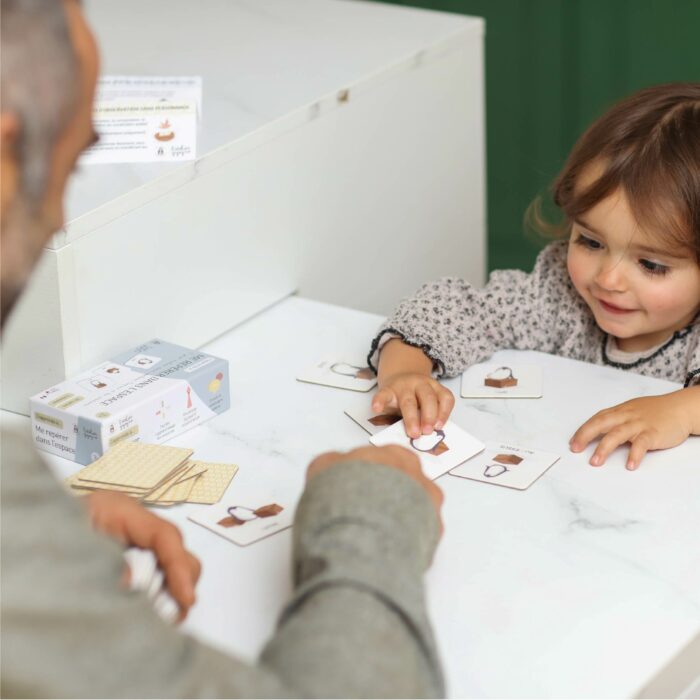 Enfant jouant au jeu éducatif pour apprendre à se repérer dans l’espace avec un adulte grâce à des cartes illustrées